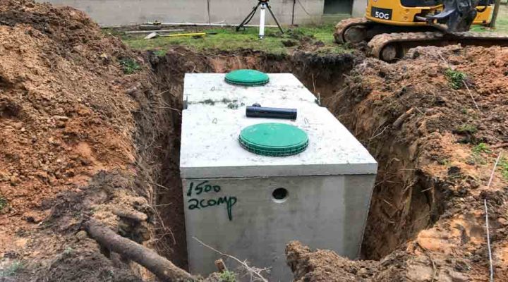 a new septic tank being installed at the backyard of a house, the mini excavator and dirt pile on the background
